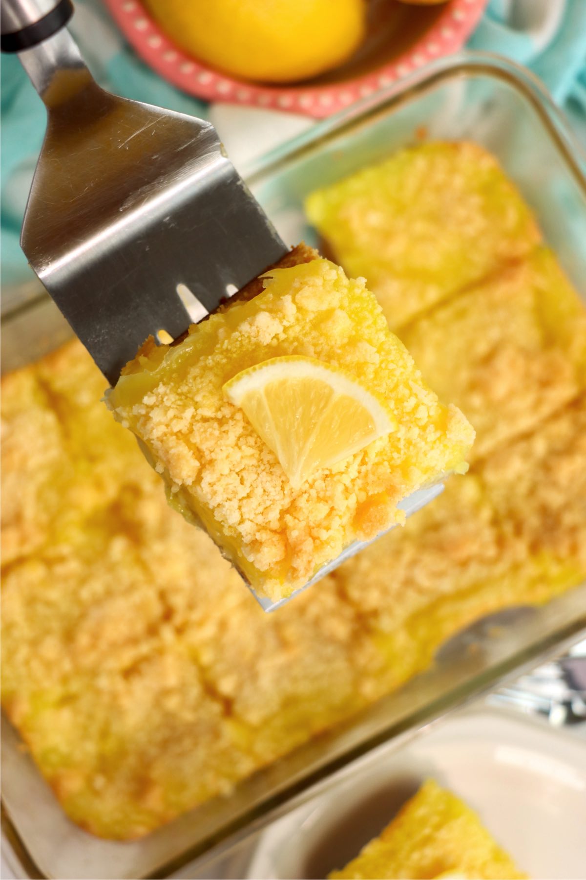 spatula holding a lemon bar garnished with a slice of lemon
