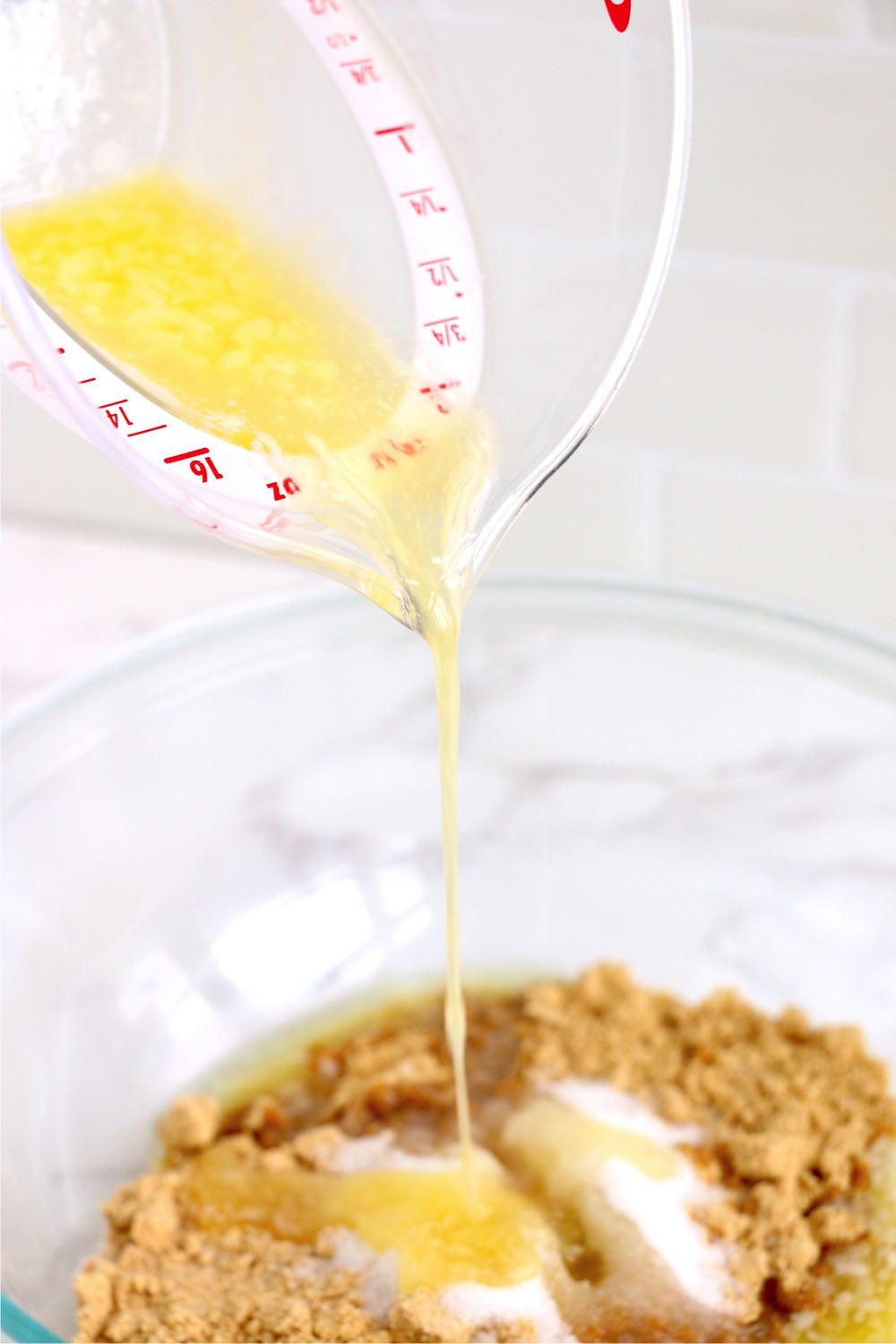 adding butter to a bowl of crushed graham crackers