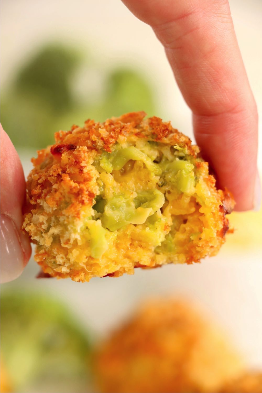 fingers holding a cheese ball with a bite out of