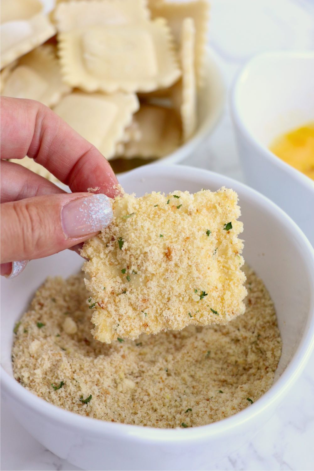 dredging ravioli in bowl of breadcrumbs
