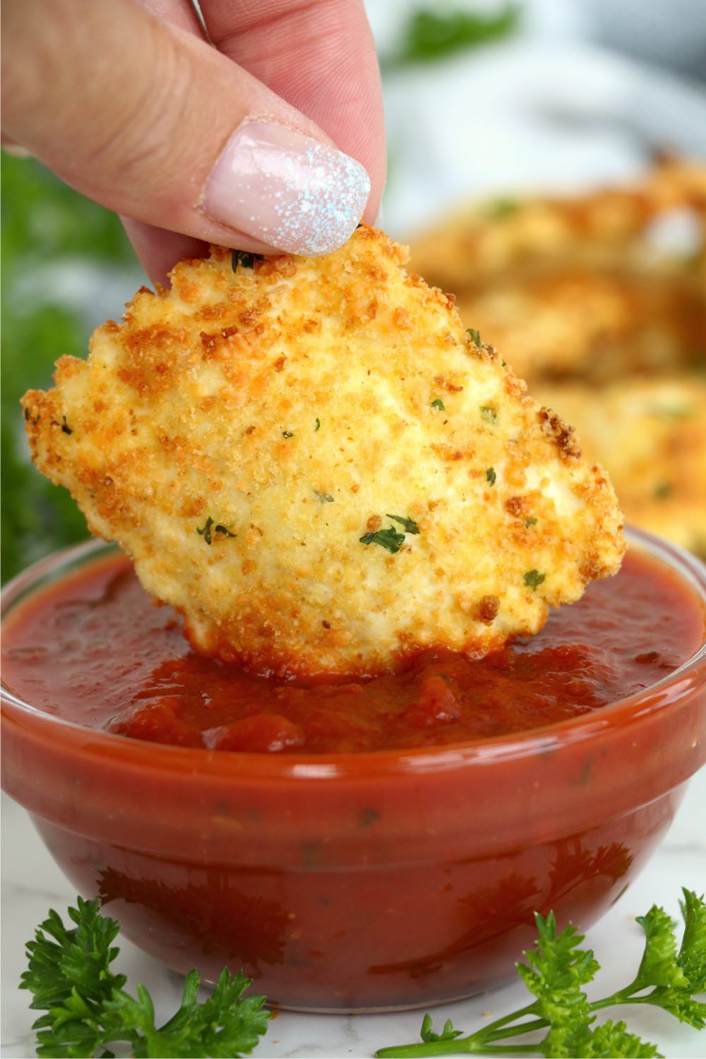 dipping piece of ravioli in marinara sauce