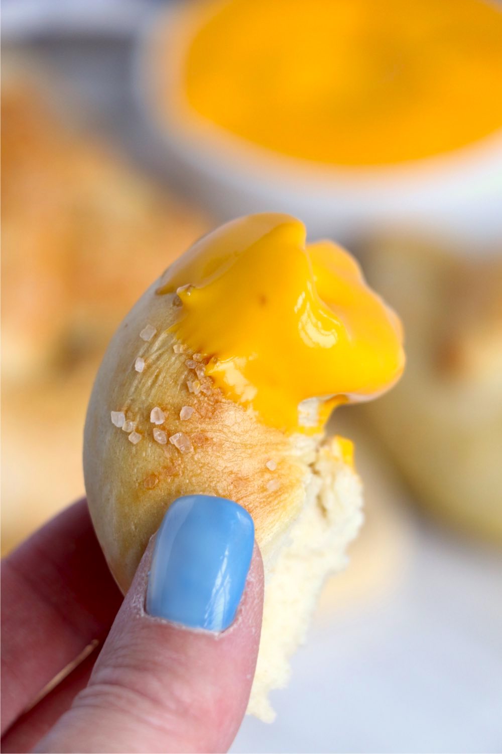 holding up a piece of pretzel with cheese sauce on it
