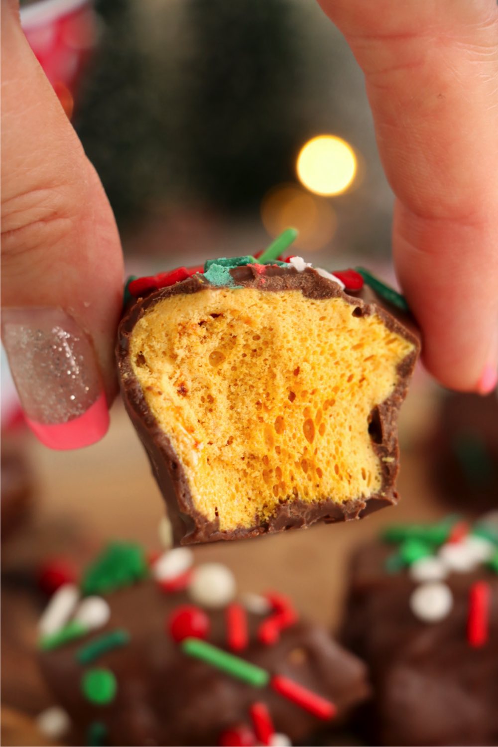 fingers holding a piece of sponge candy with a bite taken out