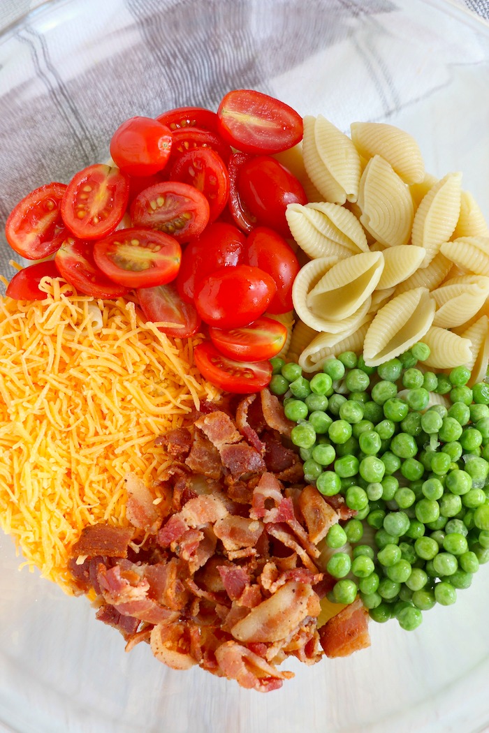 a bowl of pasta, bacon, peas, cheese and tomatoes