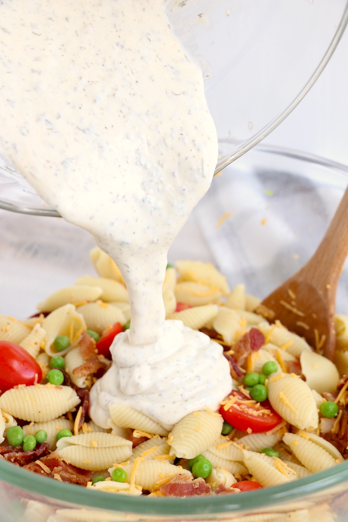 pouring ranch dressing over pasta salad