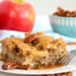 apple cake on a white plate surrounded by pecans