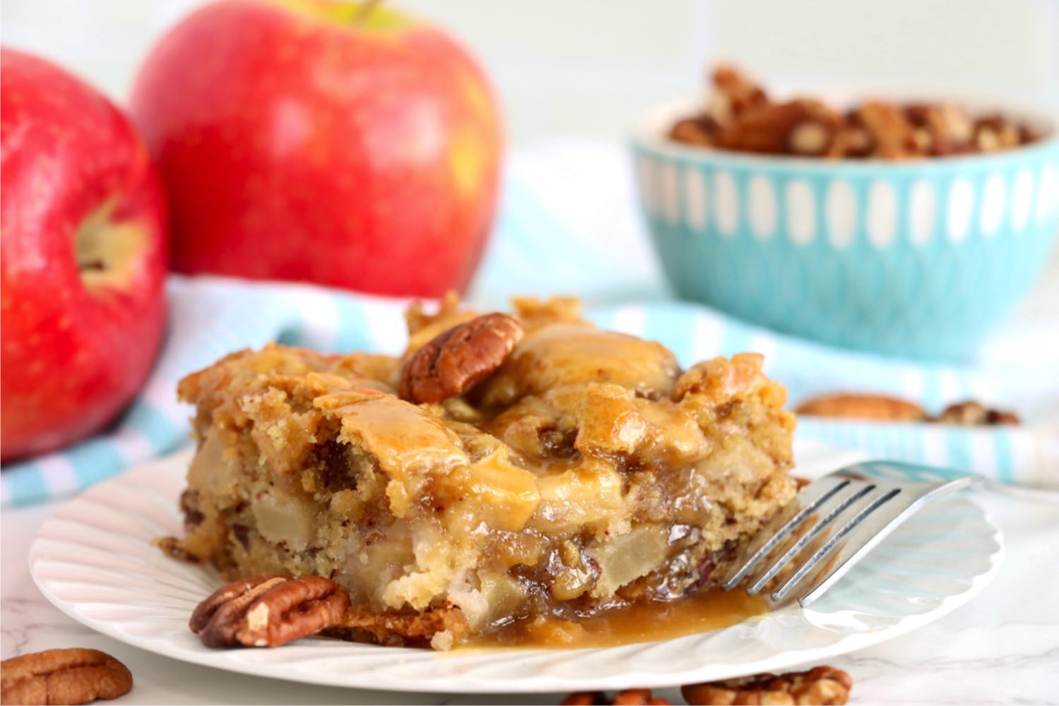 apple cake on a white plate surrounded by pecans