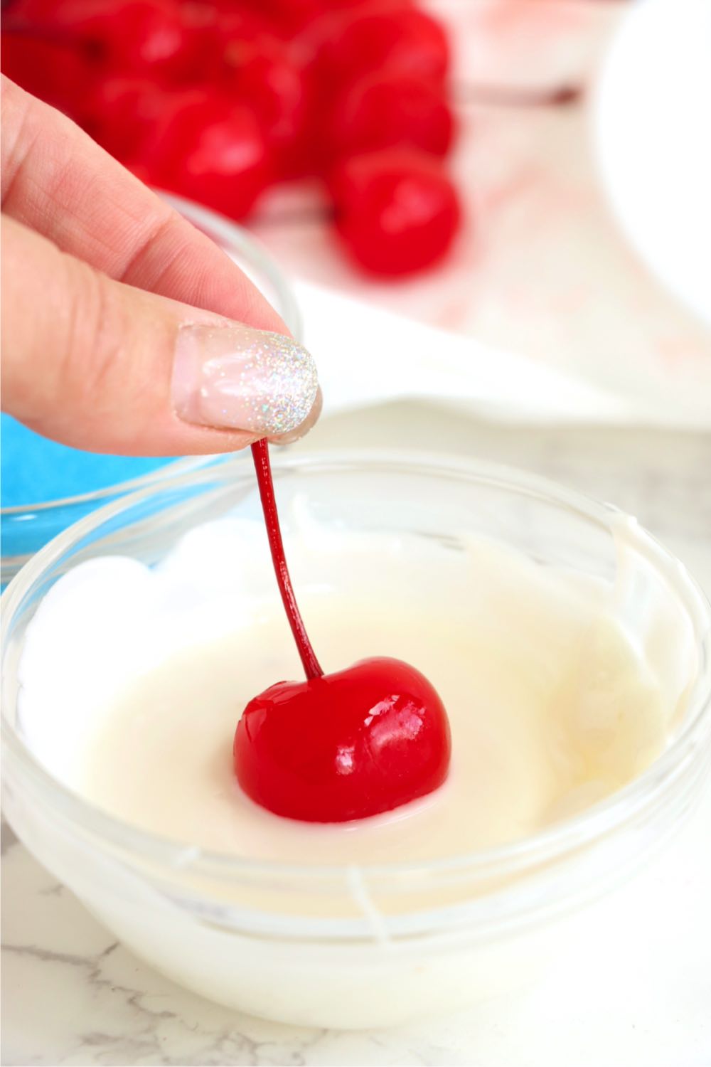 Fingers dipping a cherry into melted almond bark.