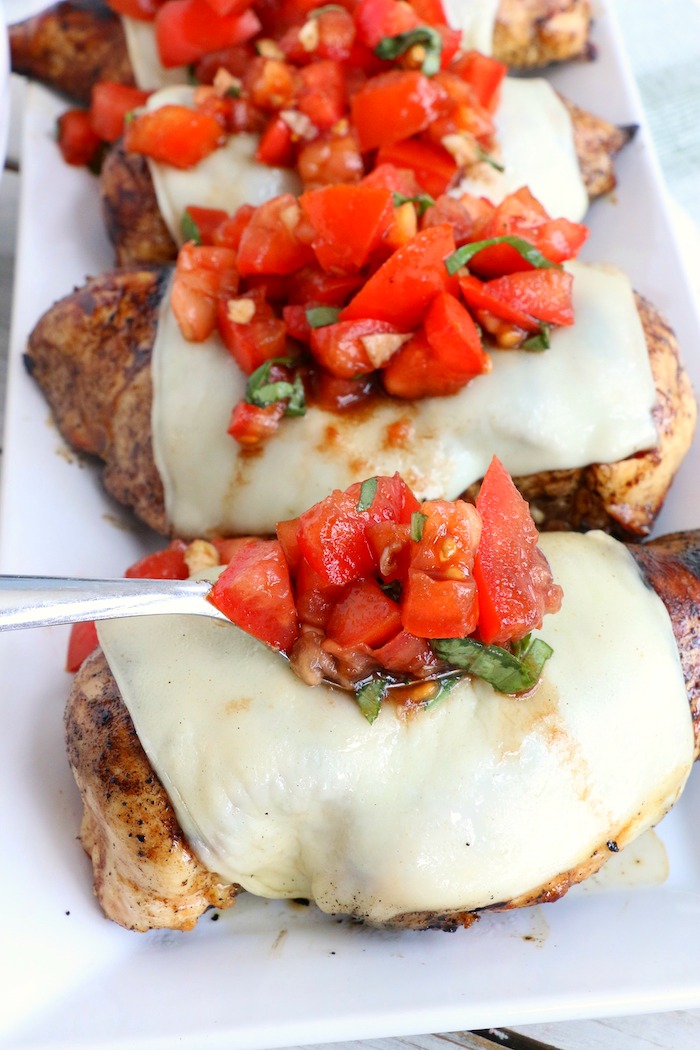 spooning bruschetta over chicken breasts with mozzarella cheese
