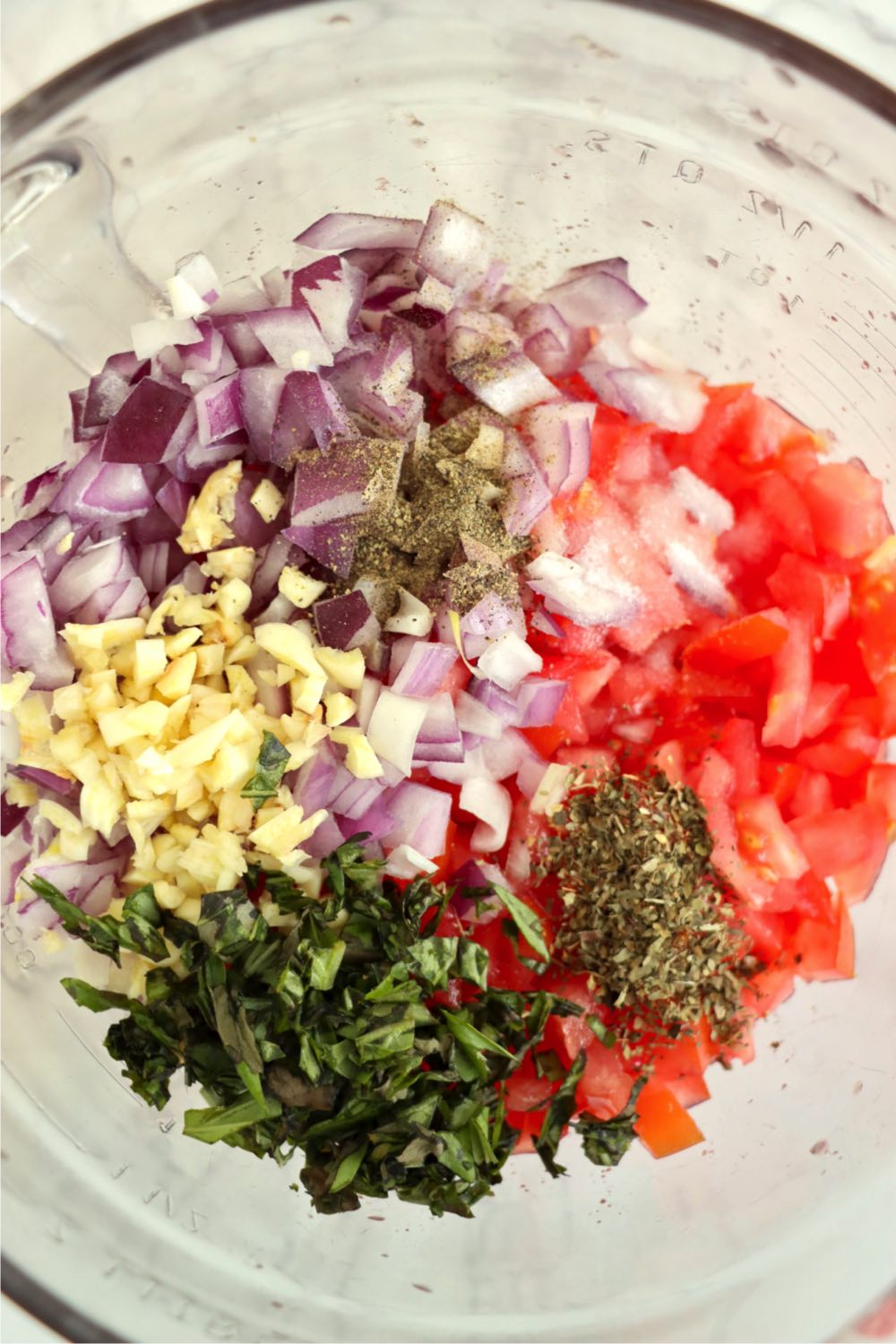 Red onion, tomatoes, garlic, basil and spices in a glass bowl.