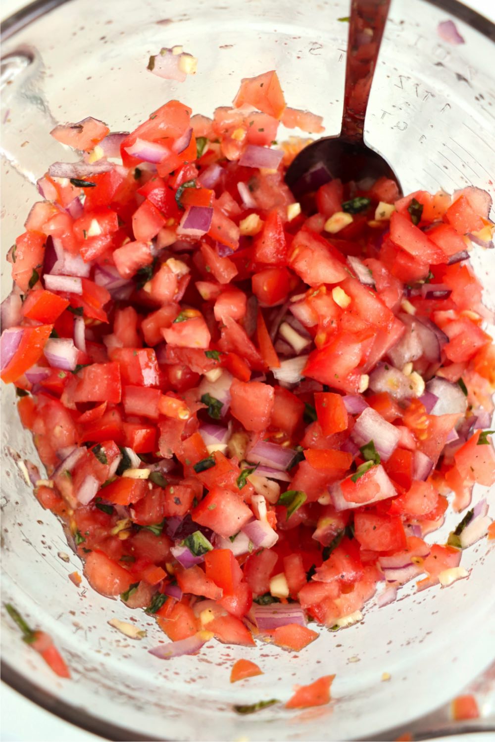 Mixing up bruschetta in a glass bowl.