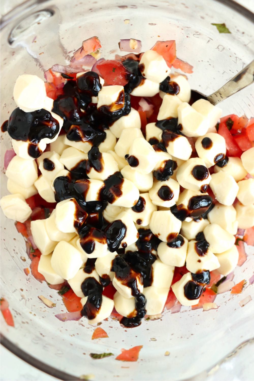 Mixing tomatoes, mozzarella and balsamic glaze in a glass bowl.