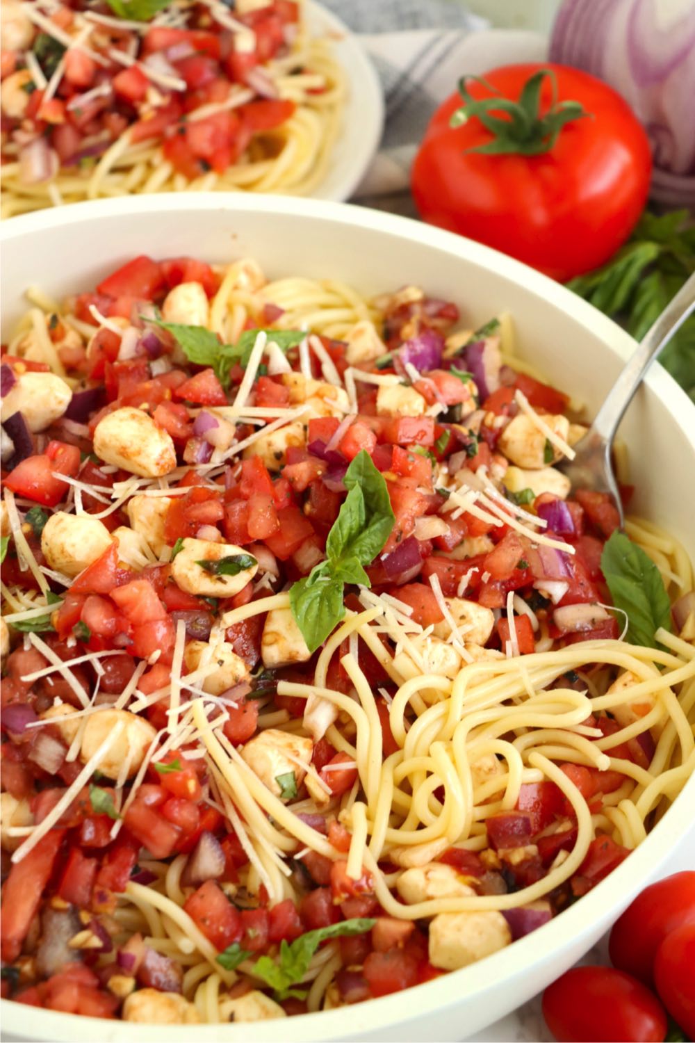 Big bowl of bruschetta cold spaghetti salad garnished with basil leaves.