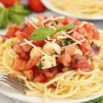 portion of spaghetti with a bruschetta topping on a white plate.