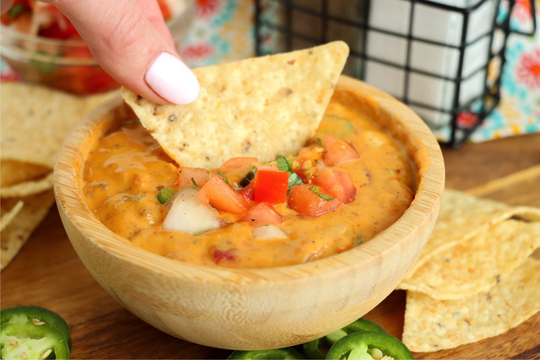 dipping a chip into a small wooden bowl of chili con queso