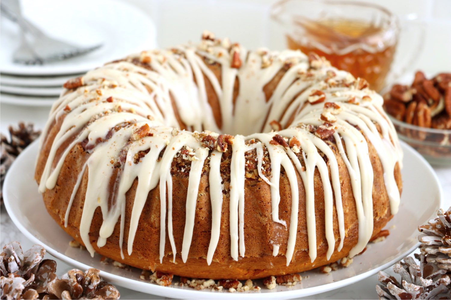 glazed rum cake on a white plate surrounded by crushed pecans