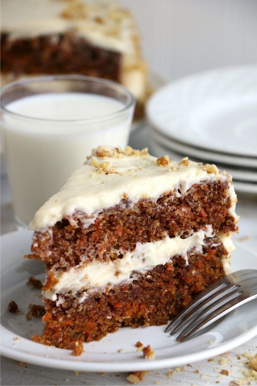 Piece of layered carrot cake on plate with glass of milk in background