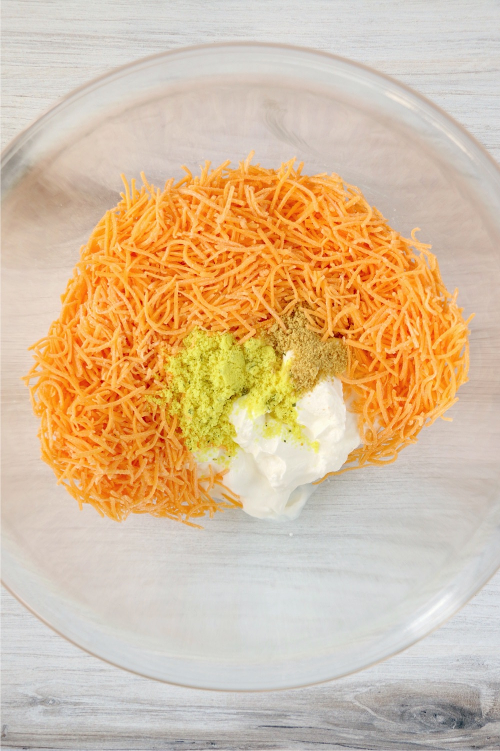 Shredded cheddar cheese, sour cream, chicken bouillon and mustard in a glass mixing bowl