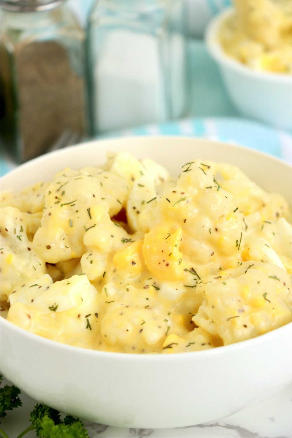 close up view of white bowl with cauliflower potato salad