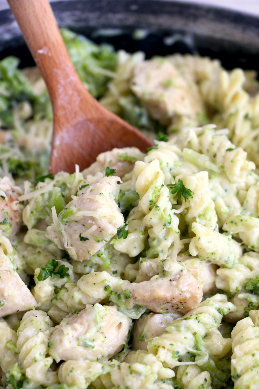 Wooden spoon scooping up some broccoli and chicken pasta