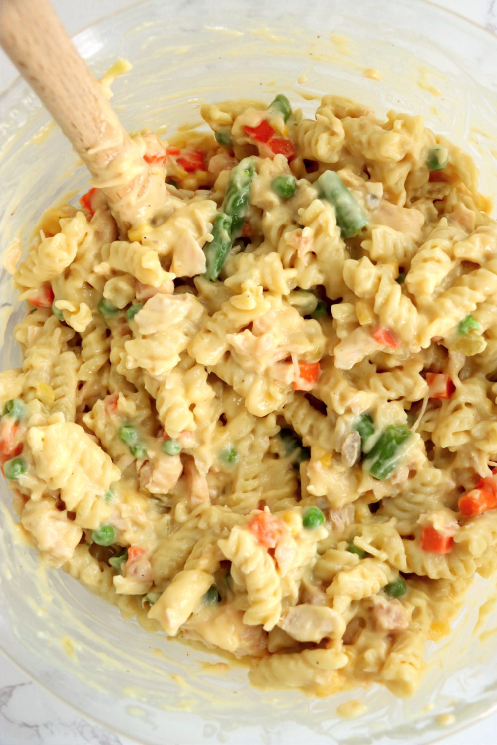 mixing together noodles, sauce and vegetables in a bowl