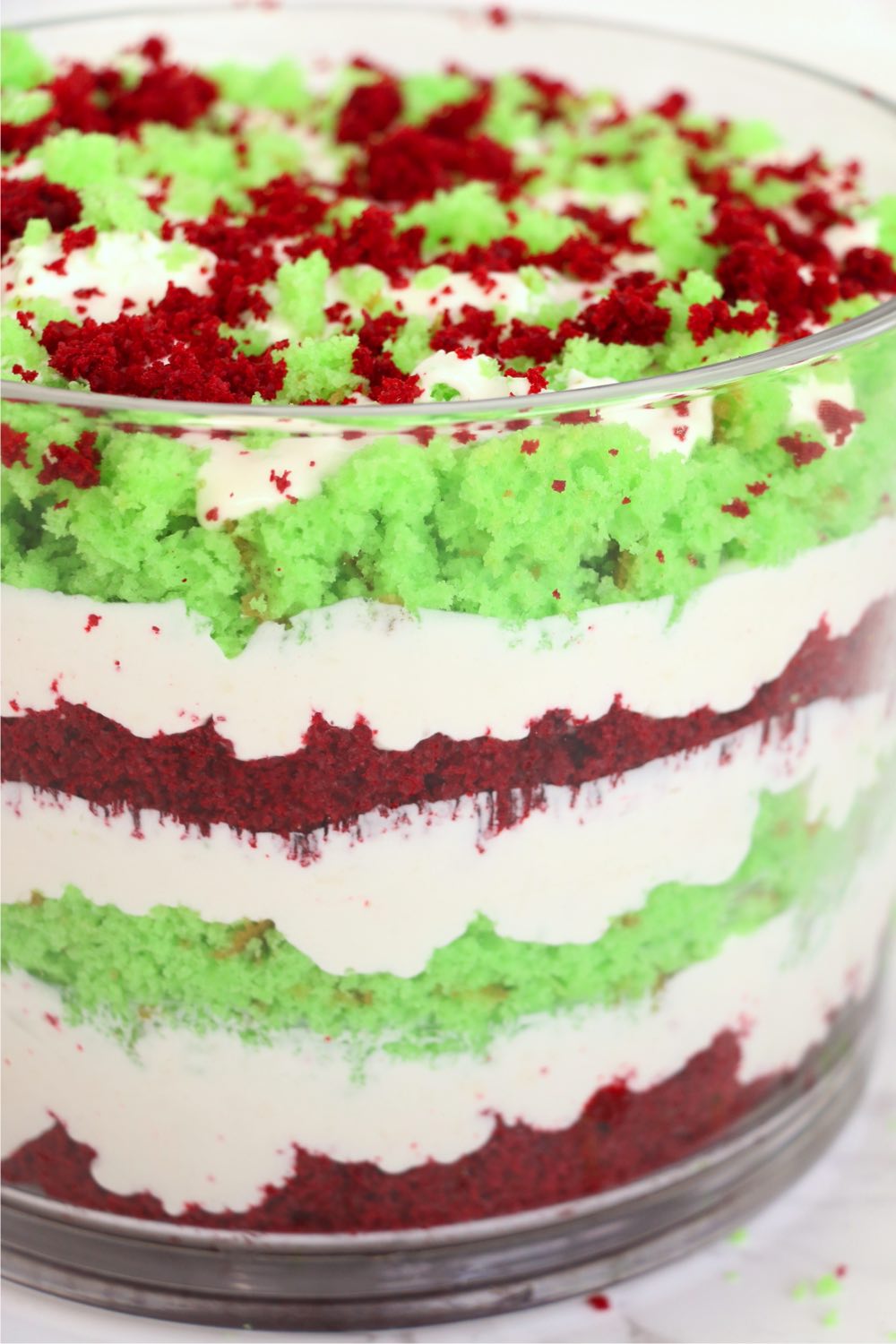 Layers of red and green cake crumbles and cream in a trifle bowl.
