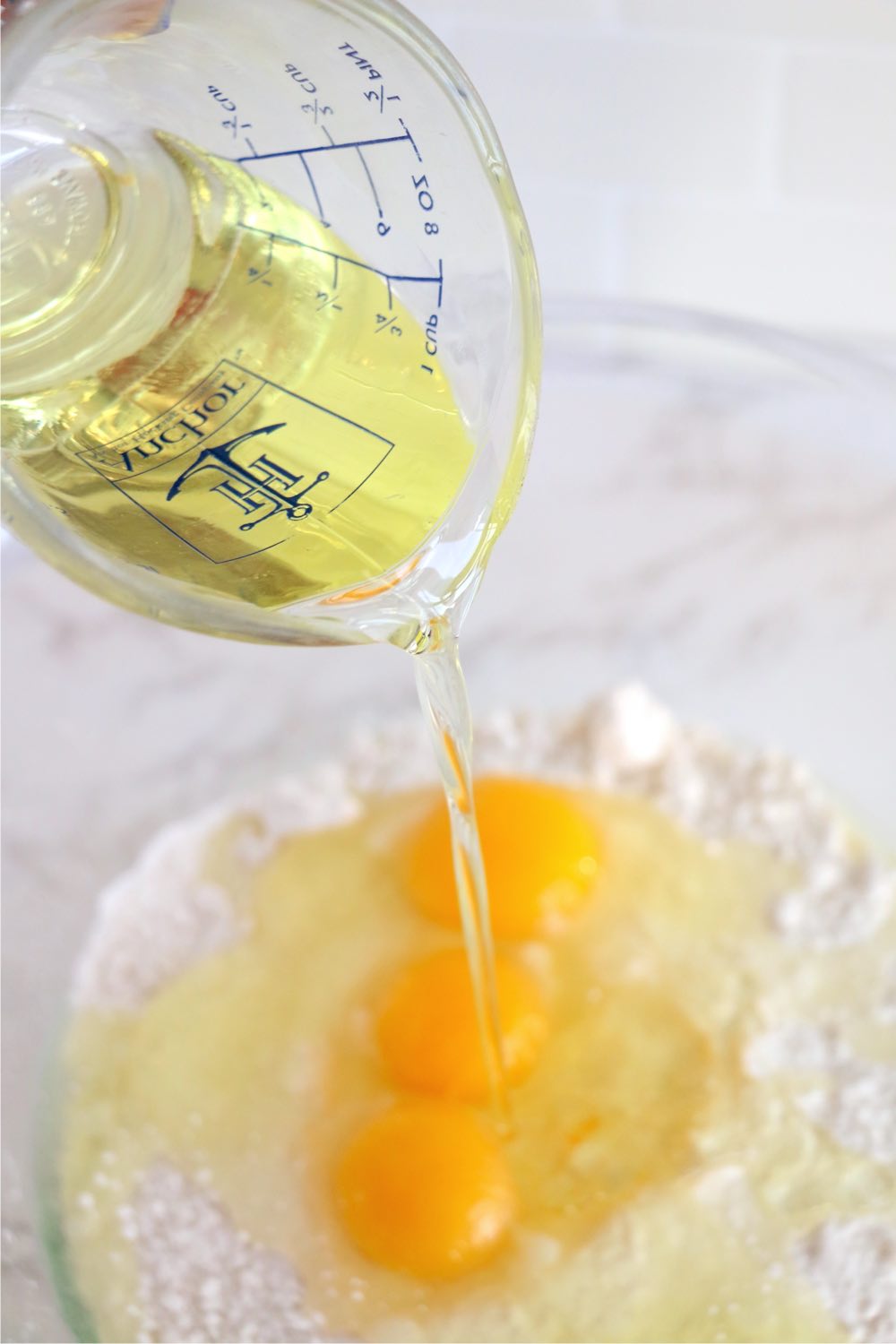 Pouring oil from a measuring cup into a bowl of eggs and flour.