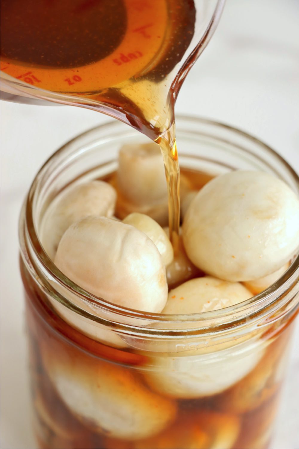 Pouring marinade mixture into a mason jar filled with fresh mushrooms