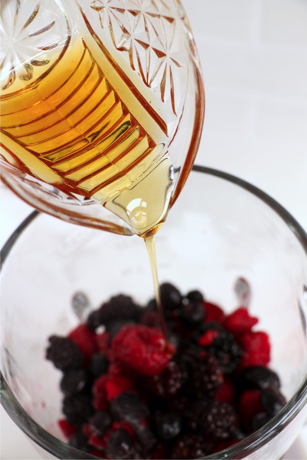 pouring maple syrup into blender filled with berries