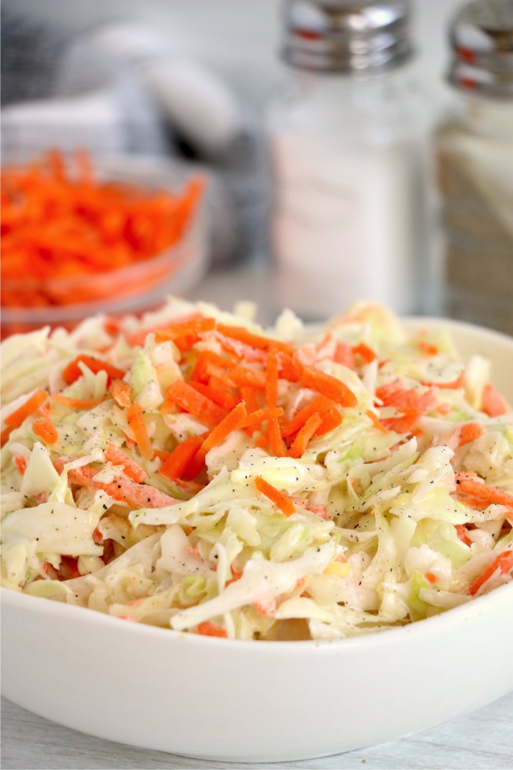 white bowl of coleslaw with salt and pepper in background