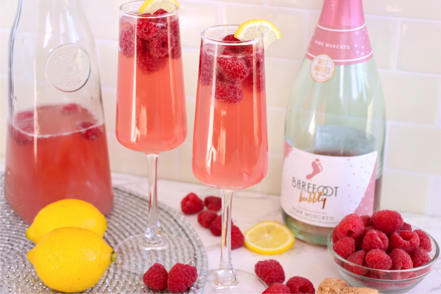 Two glasses of raspberry mimosa with raspberries and lemons.