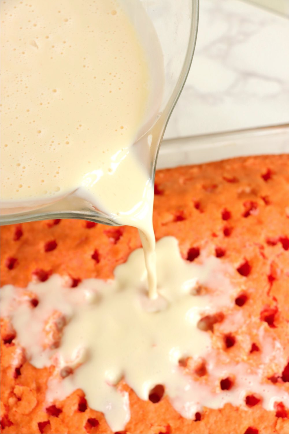 Pouring milk mixture over a strawberry tres leches cake