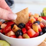 dipping a chip in a white bowl filled with fruit salsa