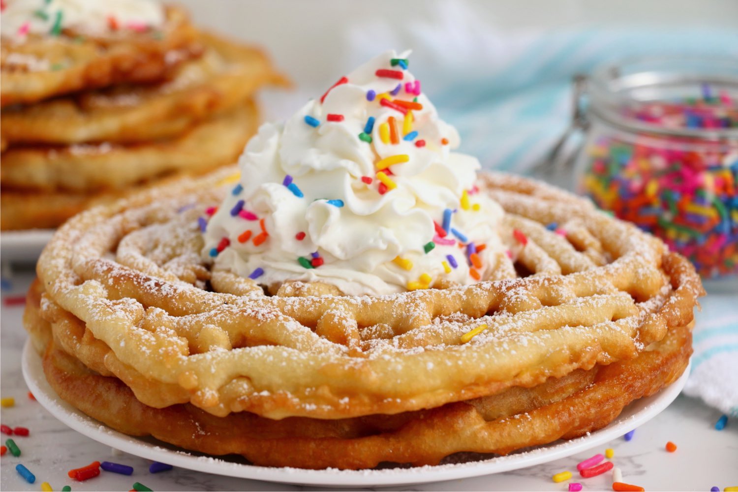 stack of funnel cakes with whipped cream and sprinkles