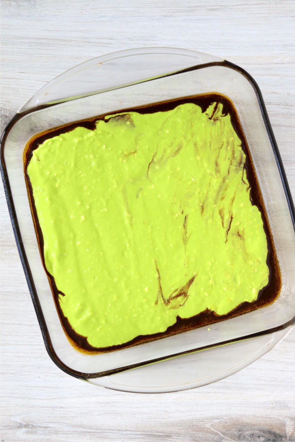 Neon green cream cheese layer on top of brownie layer in baking dish