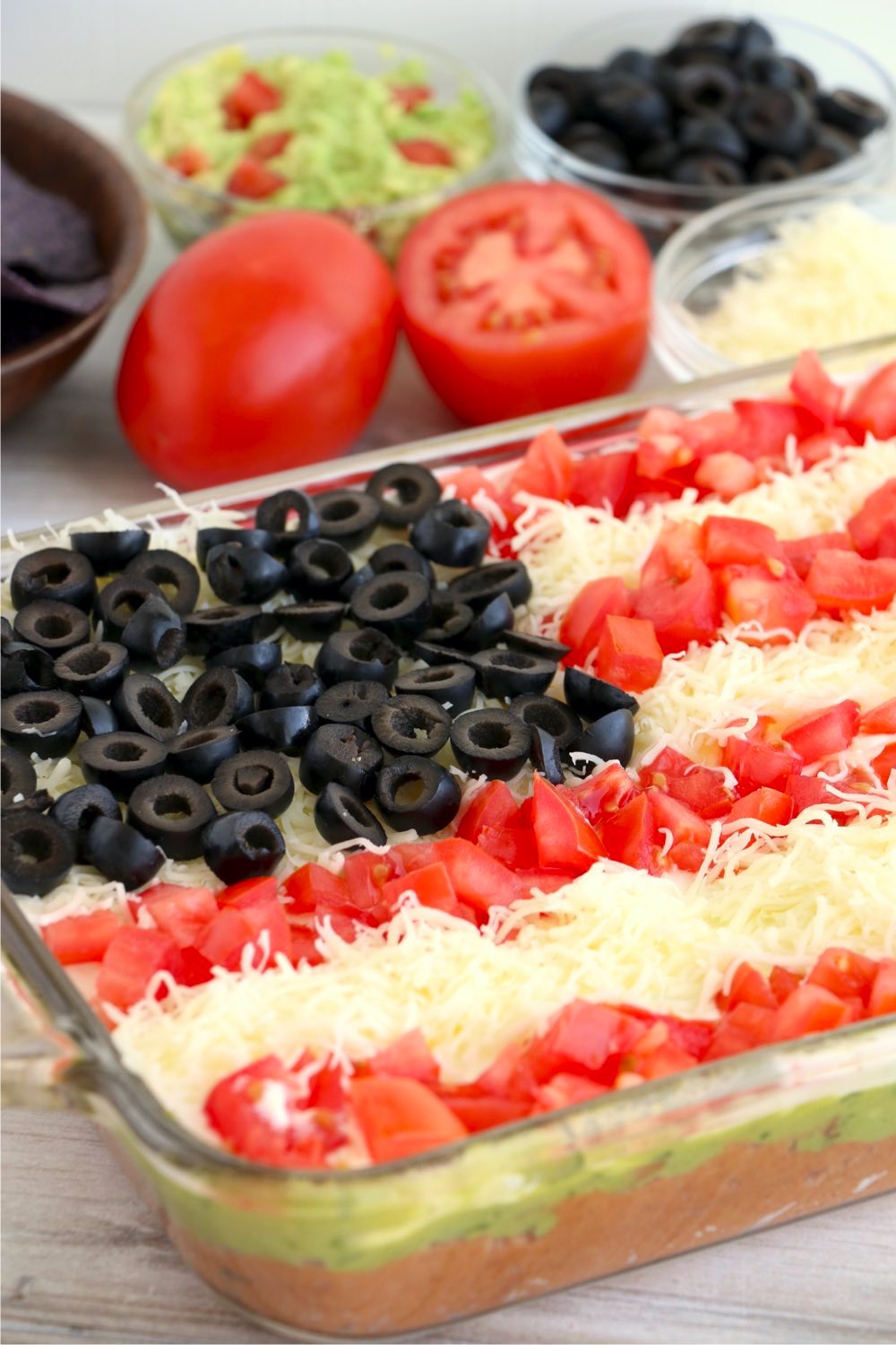pan of layered taco dip with cheese and tomatoes in background