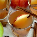 glass of apple cider garnished with apple slices and cinnamon sticks