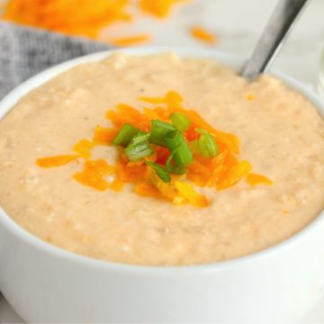 white bowl of cauliflower soup with cheese and onions