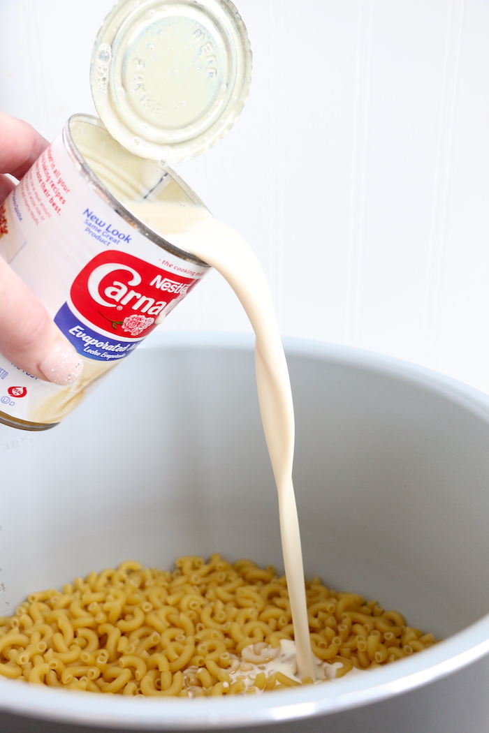 pouring evaporated milk onto noodles in cooking pot
