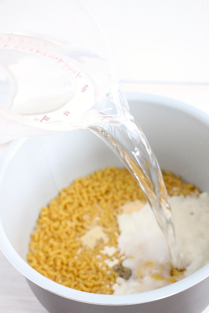 pouring water into mac and cheese mixture in Ninja Foodi cooking pot