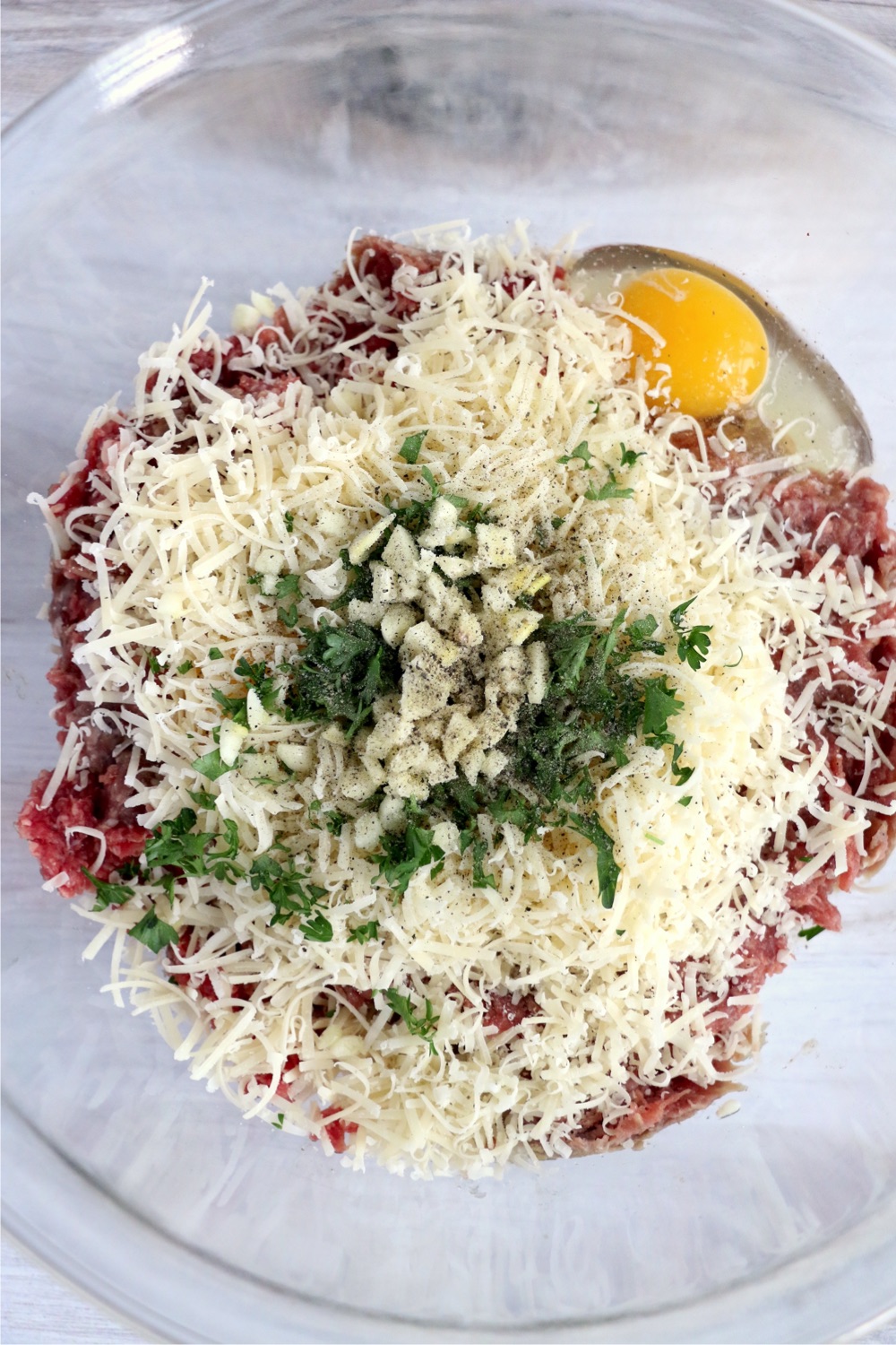 Mixing bowl filled with ground beef, ground pork, garlic, Romano cheese, parsley, salt and pepper