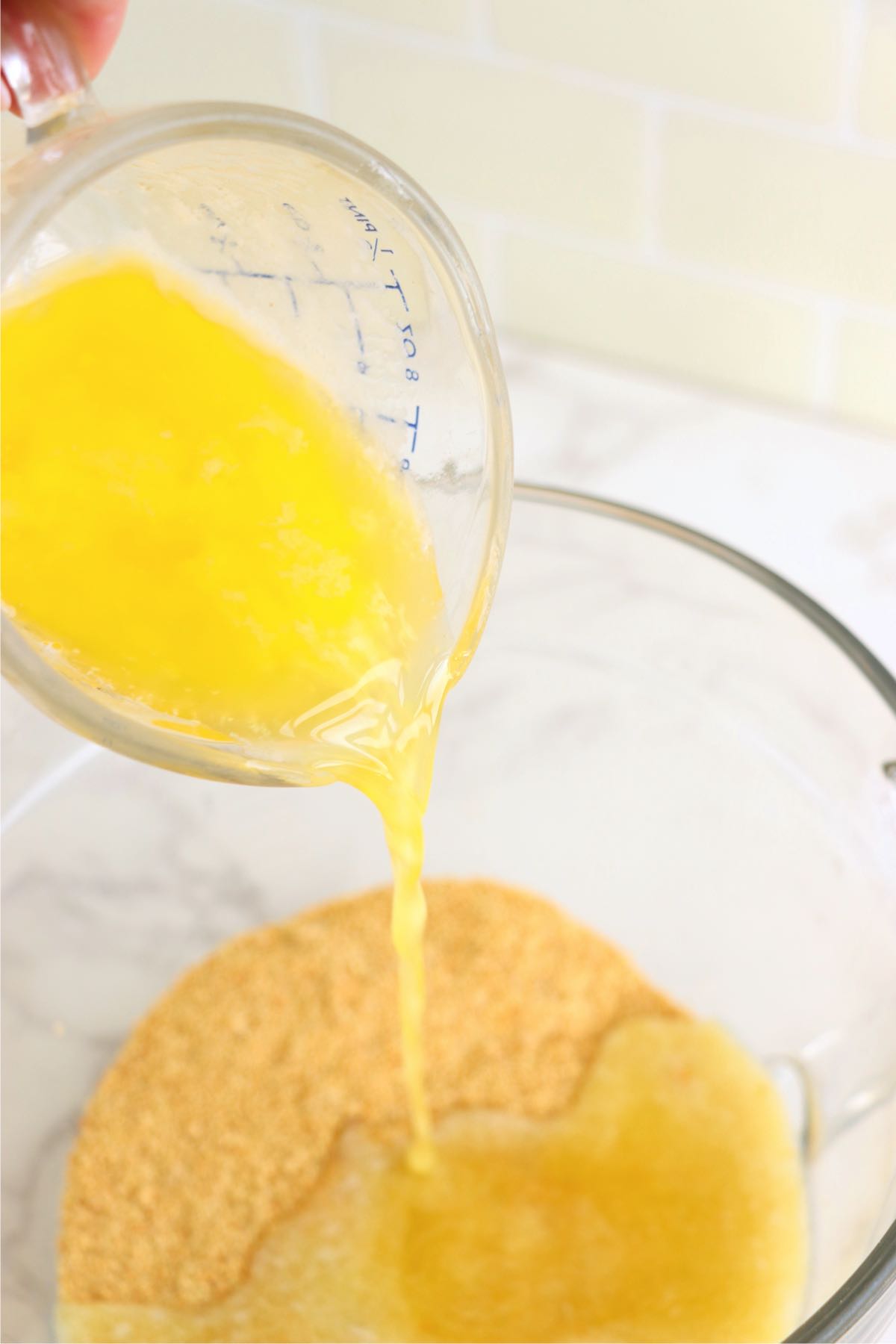 Pouring melted butter into a bowl of crushed graham crackers