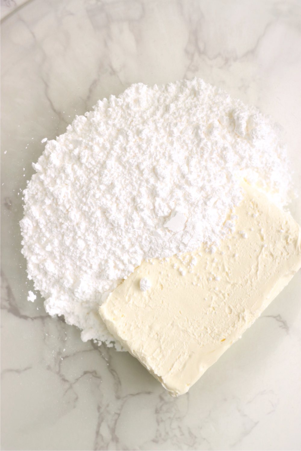 Block of cream cheese and powdered sugar in a mixing bowl.