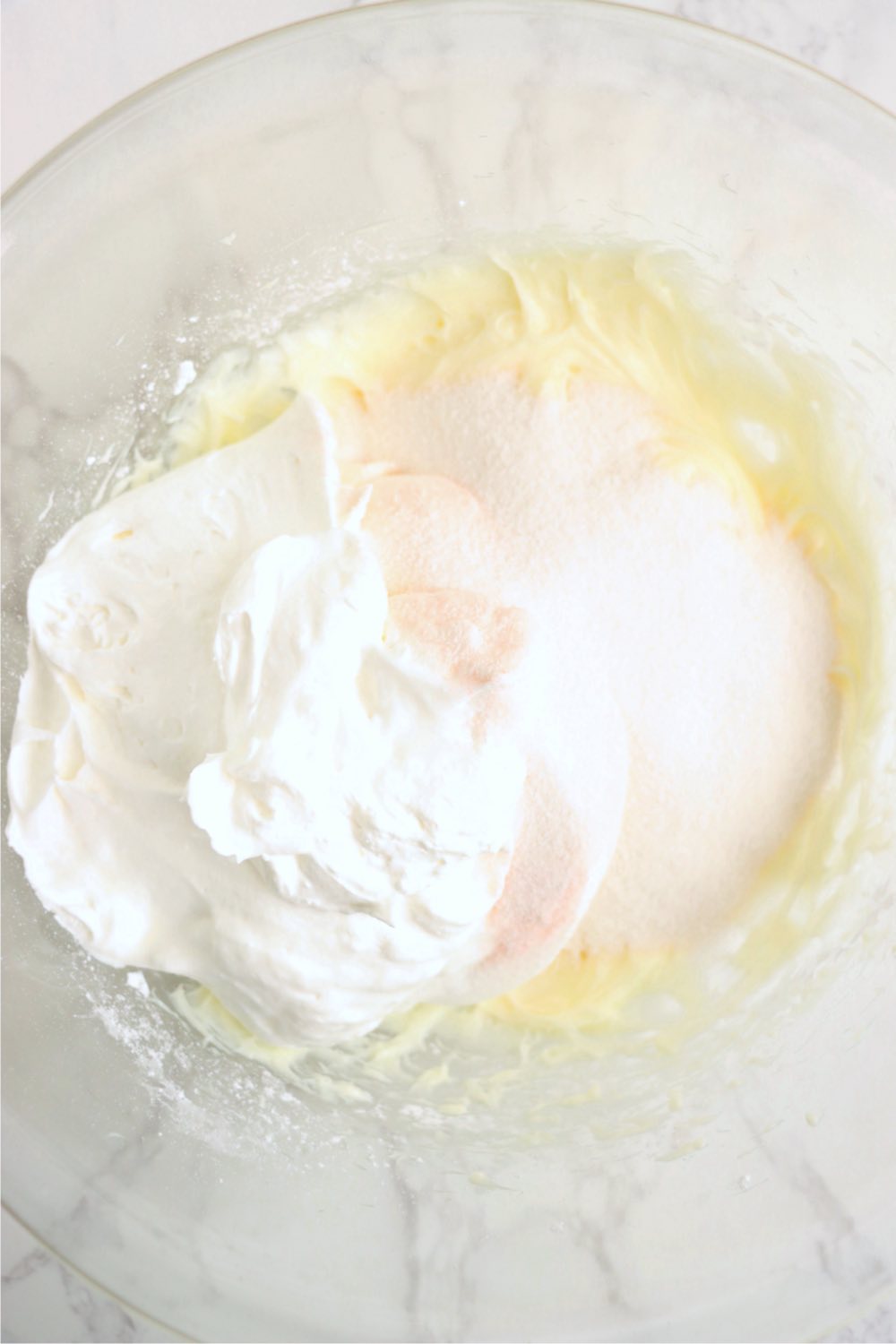 Whipped topping, peach jello powder and cream cheese mixture in a mixing bowl.