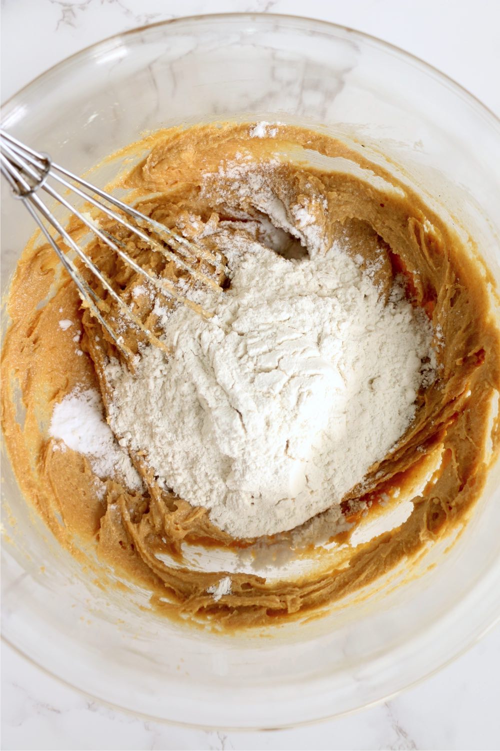 Adding flour to peanut butter in a glass bowl