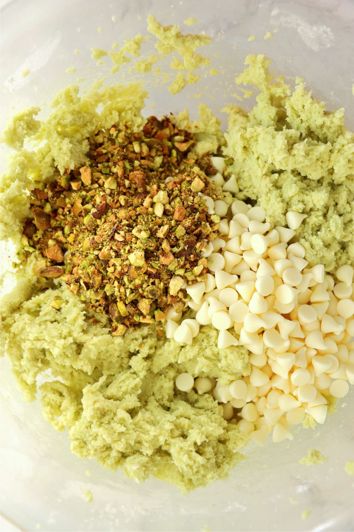 Pistachios and white chocolate chips in a mixing bowl with softened butter