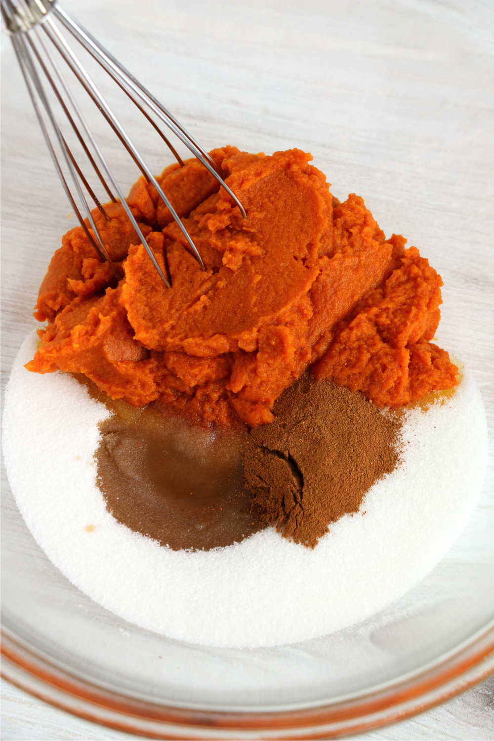 Mixing pumpkin, sugar, eggs, pumpkin pie spice, salt, and vanilla in a glass bowl.