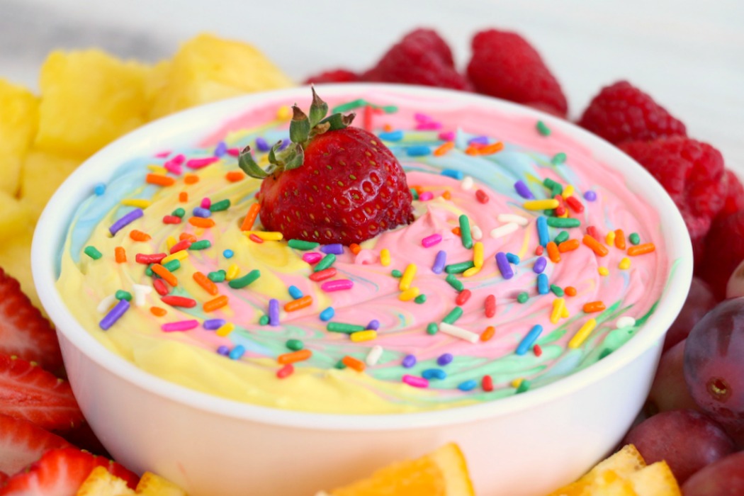 Rainbow fruit dip in bowl with sprinkles and a strawberry