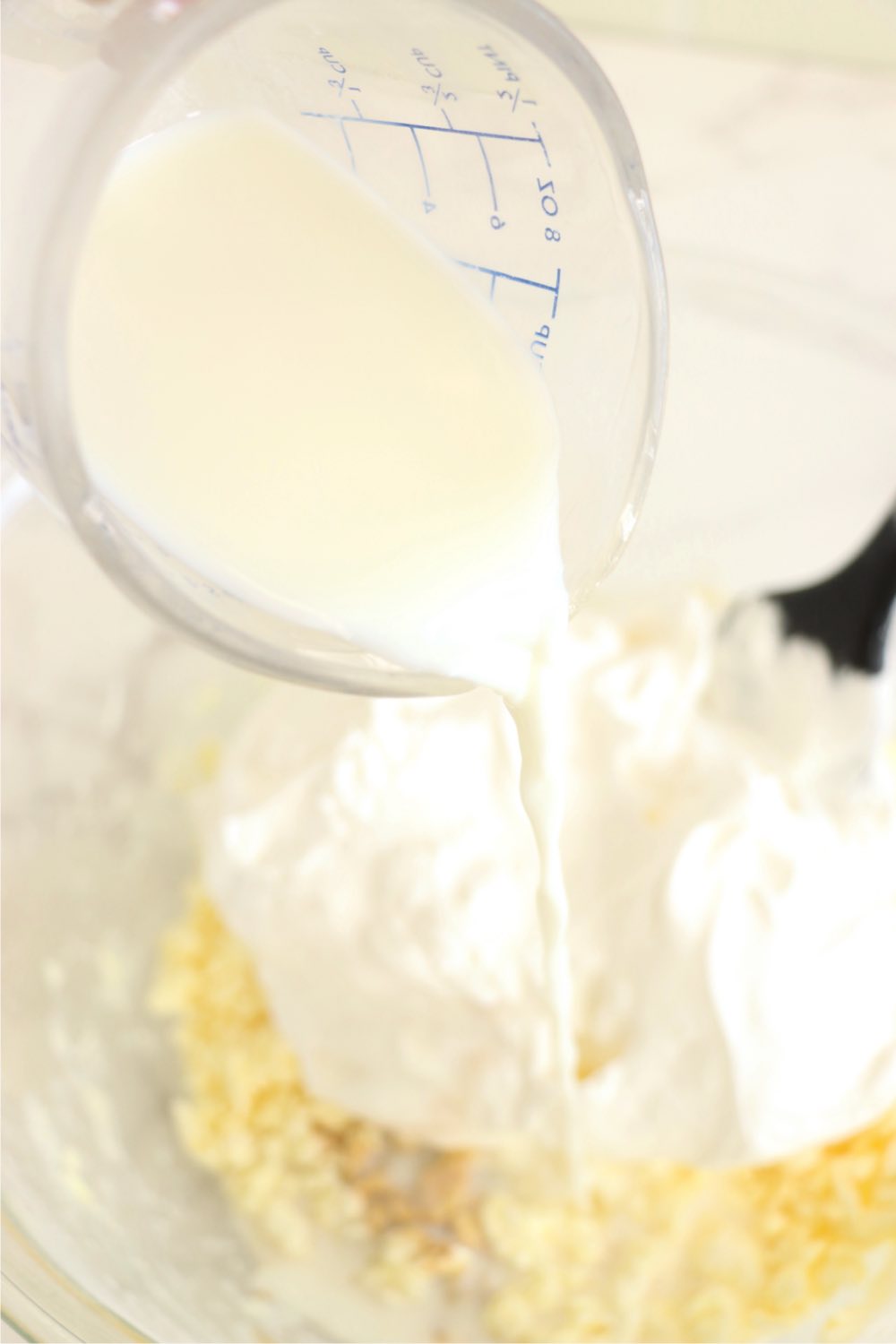 Pouring milk into a mixing bowl filled with pudding, cream cheese and whipped topping.