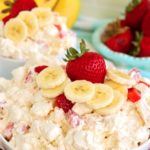 white bowl filled with a fruit fluff salad and garnished with fresh strawberries and sliced bananas.
